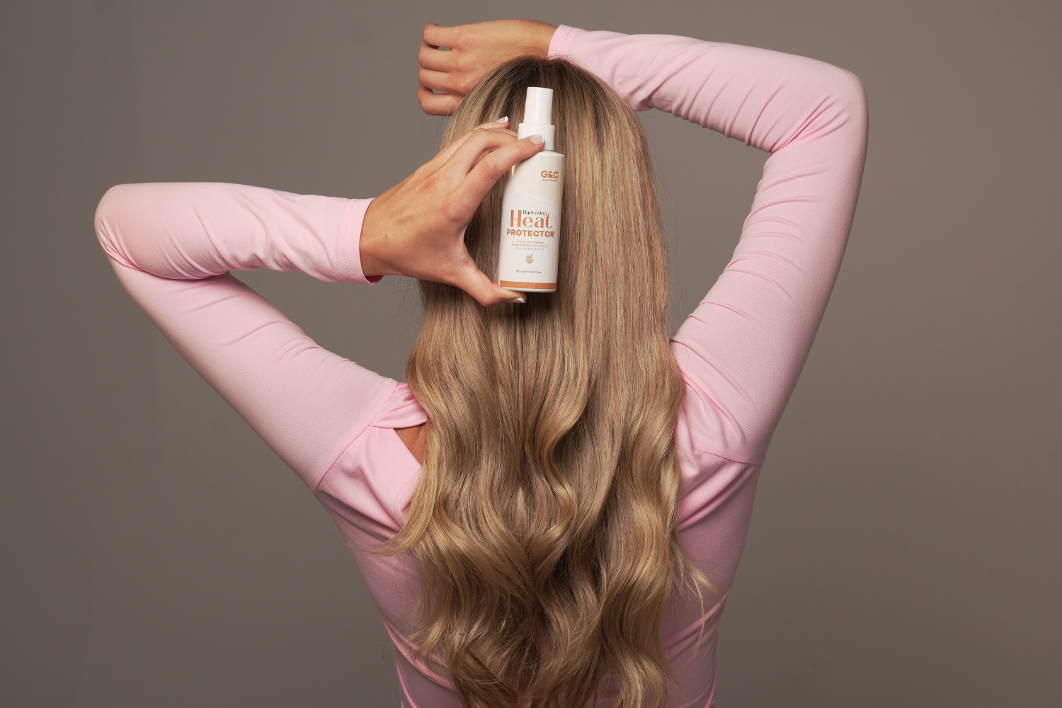 Woman holding a bottle of hair product with long blonde hair gold class g&c