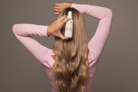 Woman holding a bottle of hair product with long blonde hair gold class g&c